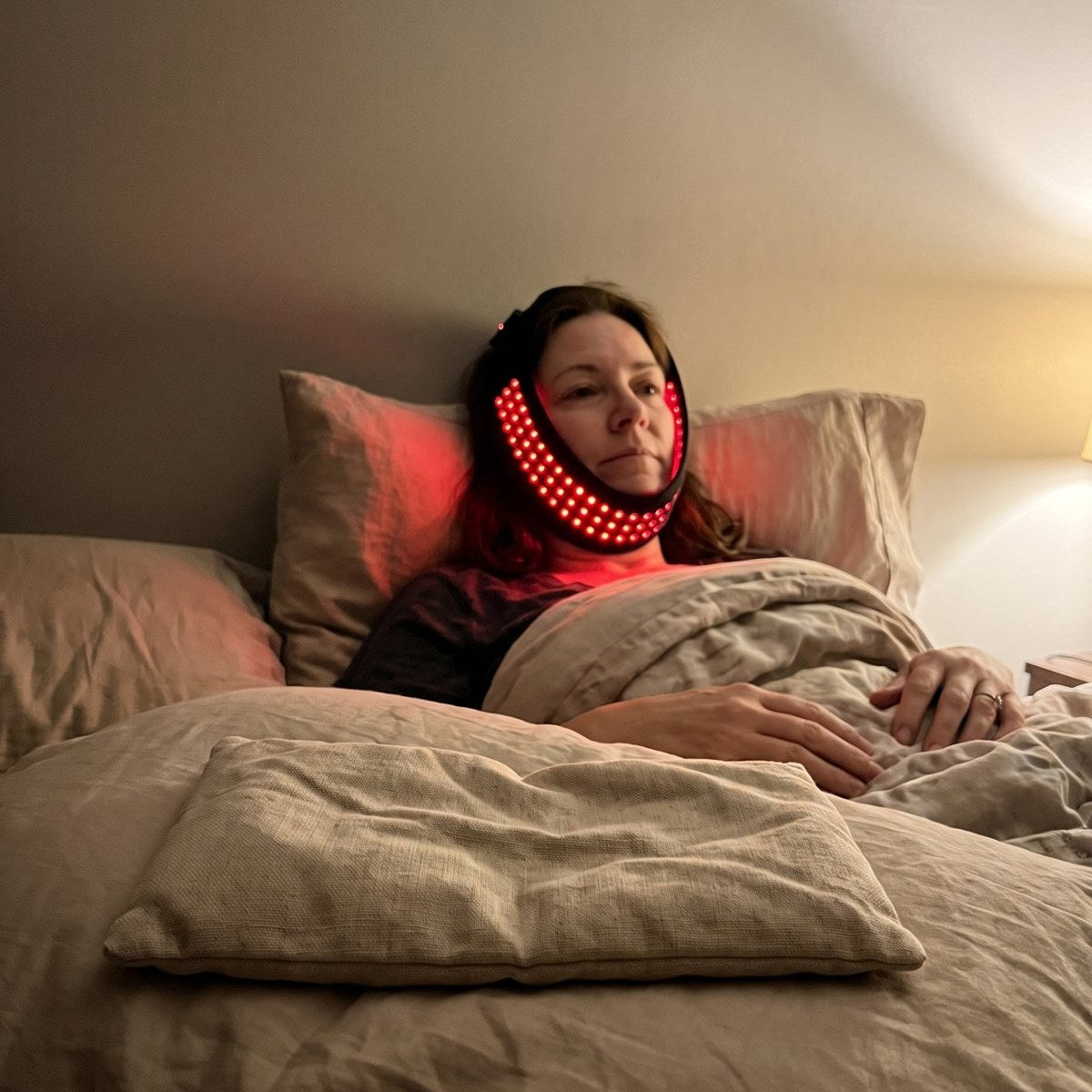 A phone photo of a gel heat pack left on a pillow, a woman behind it lying back with the jaw pad on.